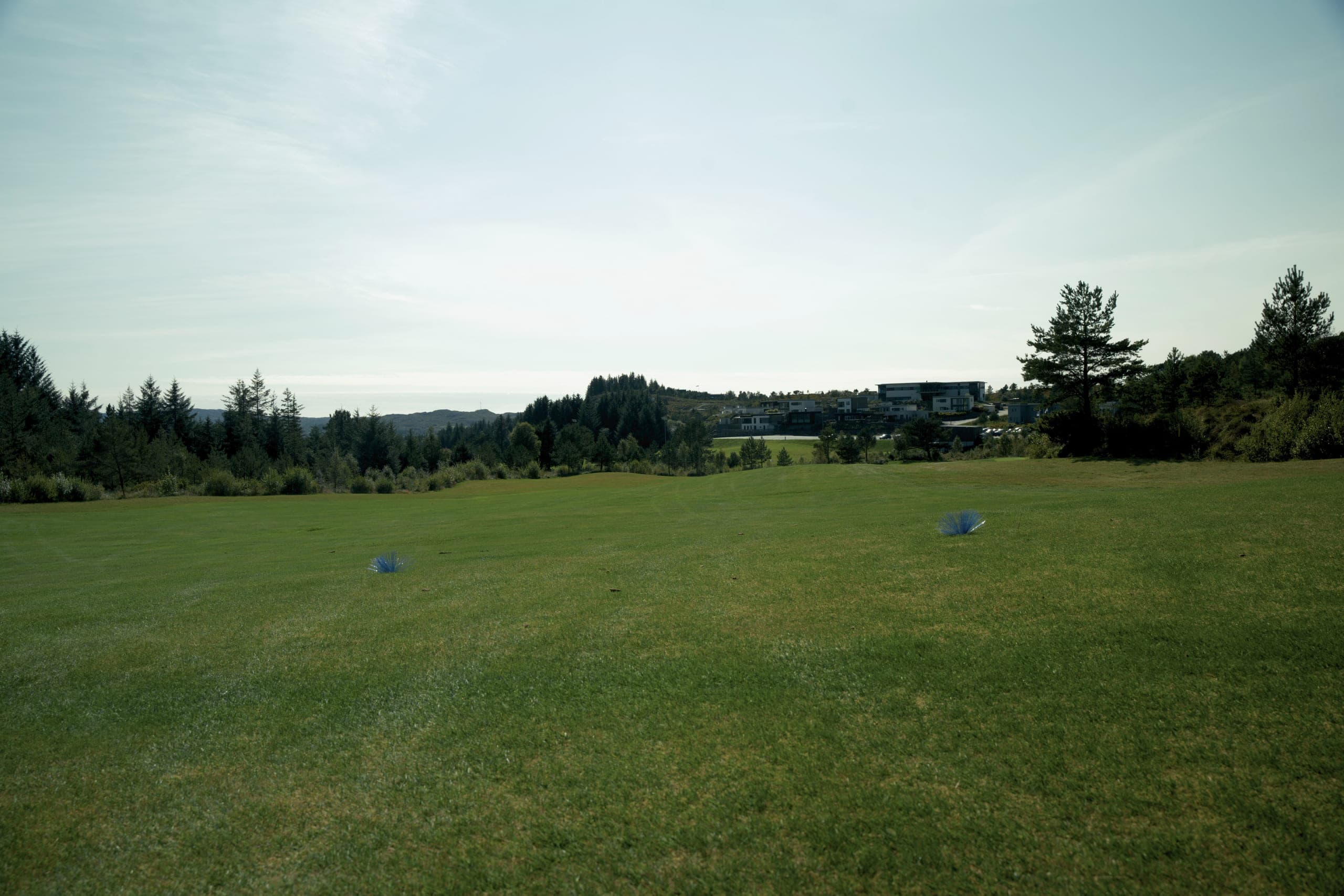 Blå utslagsmerker på Haugaland Golfbane Sveio med klubbhuset i bakgrunnen